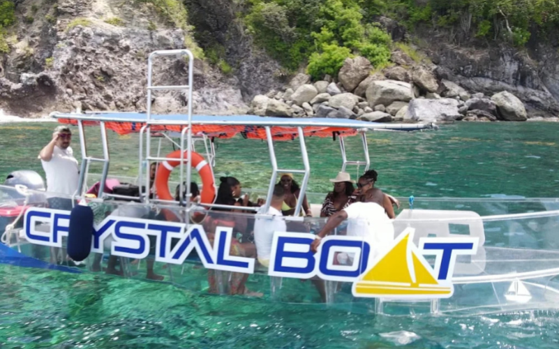 Vue extérieure du Crystal Boat naviguant le long des falaises de Deshaies avec des passagers à bord.