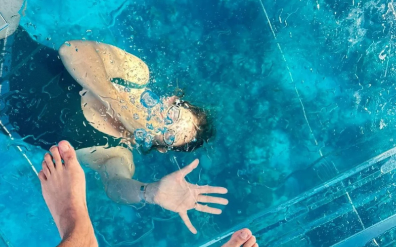 Vue spectaculaire à travers le plancher de verre montrant un baigneur nageant sous la coque du bateau transparent.