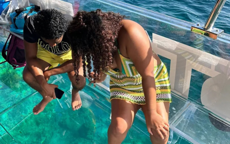 Couple observant attentivement les fonds marins et l'eau turquoise à travers la coque vitrée du bateau transparent.